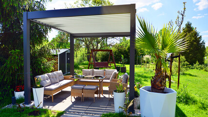 Fototapeta na wymiar Modern aluminum pergola with stylish garden furniture in a beautiful garden.
