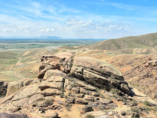 eroded sandstone outcrop with layered rock formations in arid foothills under blue sky, ideal for...