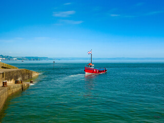 Red boat leaving pier after unloading passengers (Caldey Island, Tenby, Wales, United Kingdom)