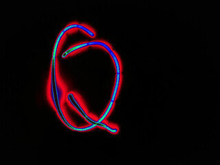 Glowing English letter Q. On a black background with colored neon lines, a letter of the English alphabet is written by hand. The letter glows pink-red, creating a green-blue halo around it.