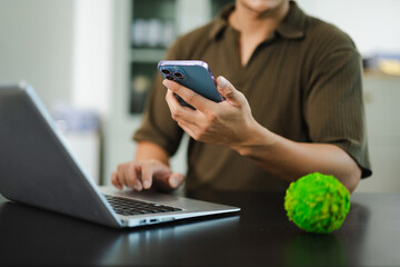 Young Asian man holding a globe and smartphone at desk, symbolizing green technology, sustainability, eco business, and clean energy innovation