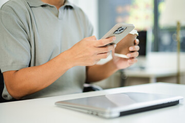 Asian man holding coffee and smartphone, working in modern office with laptop. Perfect for lifestyle