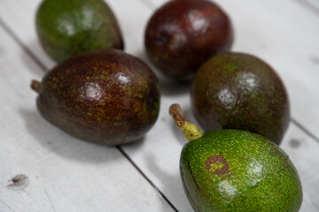 A fresh arrangement of whole and halved avocados displayed on a white wooden table, highlighting...