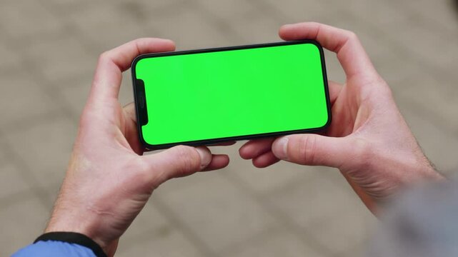 NEW YORK - December, 19 2020: Close up young man holding a smartphone touching phone with horizontal green screen phone on background street. Message business male device digital equipment internet