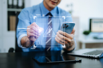 Businessman holding smartphone with digital alert icon. Concept of cyber risk, security warning, data protection, and tech threats