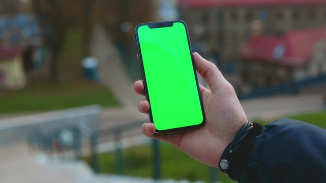 NEW YORK - December, 19 2020: Close up hands man using phone with vertical green screen background street city blurred internet chrome outdoor. Cellphone media device modern cellular. Slow motion