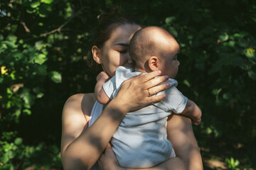 Young Asian mother is holding cute boy son and kissing his cheeks with love and tenderness. Newborn baby cute and cheerful. Concept of motherhood parenting. 