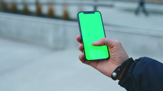 NEW YORK - December, 19 2020: Close up hands man using phone with vertical green screen background street city blurred internet chrome outdoor. Cellphone media device modern cellular. Slow motion