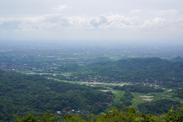 Fototapeta premium Panoramic View of Green Hills and Farmlands Under Cloudy Sky