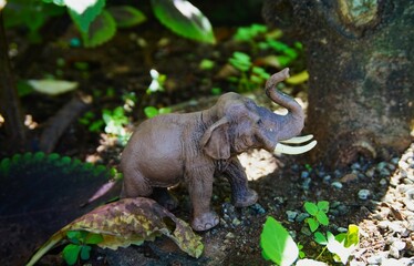 small plastic elephant toy photographed on rocks and bushes to make it look like a real elephant