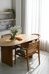 Peaceful interior room inside home features wooden dining table and cane chair bathed in soft daylight and warm sunlight