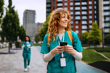 Healthcare professionals in scrubs walk through urban park while checking mobile devices in the...