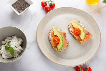 Whole grain toasts with avocado, salmon and cherry tomatoes on white marble background with fresh ingredients. Top view. Concept of healthy breakfast and natural lifestyle
