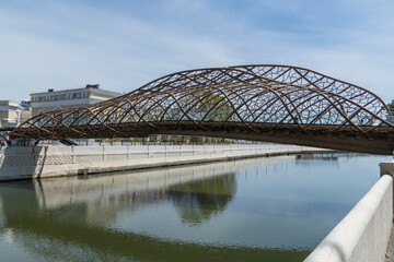 Modern, intricately designed metal bridge arches gracefully over calm river  Sochi, reflecting its...