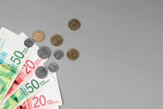 Israel currency 100 and 50 New Israeli shekel (NIS) banknotes alongside agorot coins, on grey background, concept of inflation, economic crisis, rising prices, and financial management.