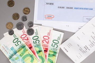 Israel currency New Israeli shekel (NIS) banknotes and agorot coins, with bills for electricity,...