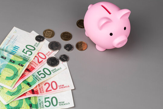 Israel currency New Israeli shekel (NIS) banknotes and agorot coins and a piggy bank, concept of saving money, inflation, economic crisis, rising prices, and financial management.