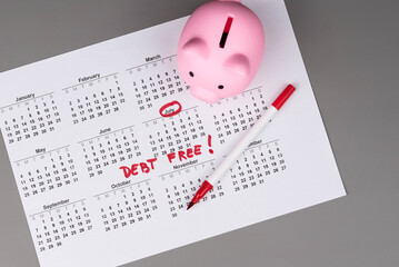 Piggy bank on calendar with the words 'Debt Free' written on it, symbolizing saving money, financial freedom, and achieving a debt-free lifestyle. Concept of financial independence and budgeting.