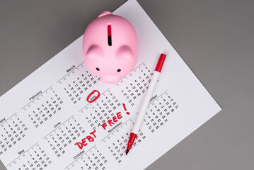 Piggy bank on calendar with the words 'Debt Free' written on it, symbolizing saving money, financial freedom, and achieving a debt-free lifestyle. Concept of financial independence and budgeting.