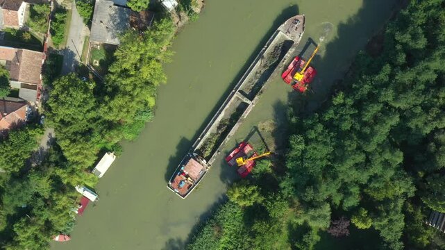 Above top view, dolly move upwards over two excavators dredge as they dredging, working on river, canal, deepening and removing sediment, mud from riverbed in a polluted waterway.