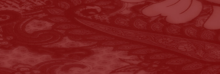 Blurred image of richly textured red fabric with artistic paisley and floral designs, blending bold...