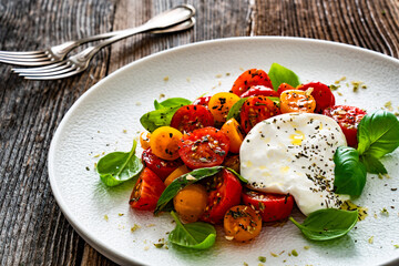 Caprese salad - cherry tomatoes, fresh basil leaves and burrata cheese on wooden background	