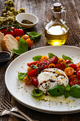 Caprese salad - cherry tomatoes, fresh basil leaves and burrata cheese on wooden background	