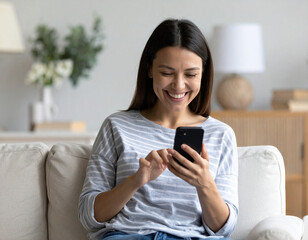Happy Relaxed Young Woman Sitting on Couch Using Smartphone and Laughing Cheerfully