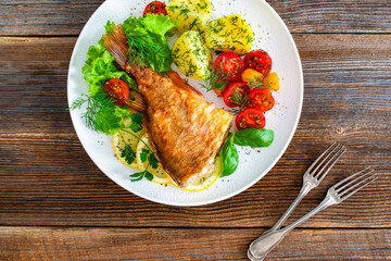 Fried atlantic redfish with boiled potatoes and tomato salad on wooden table	