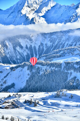 Red hot air balloon in blue sky in french Alps by winter
