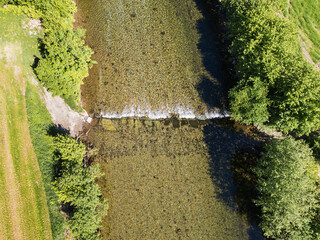 Aerial photography: a serene top-down view of a crystal-clear river with a small weir in Norway, surrounded by lush green vegetation."