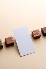 Minimal overhead shot of chocolate squares and blank square card on beige background, elegant candy dessert mockup composition