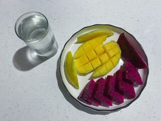 A plate of healthy mango and dragon fruit slices with a glass of water. Top view.