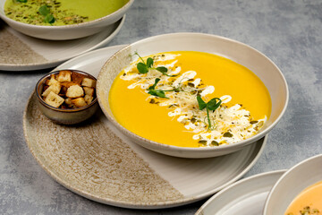 Vegan sweet potato soup in a bowl decorated with cream, pumpkin seeds and microgreens, with croutons next to it on a gray background, top view. Vegan or vegetarian food. Healthy dinner or lunch.