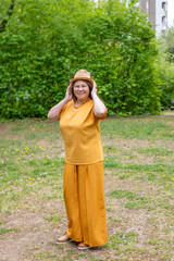 Confident Happy mature woman in yellow outfit, smiling gently, with hat, in mustard clothing...