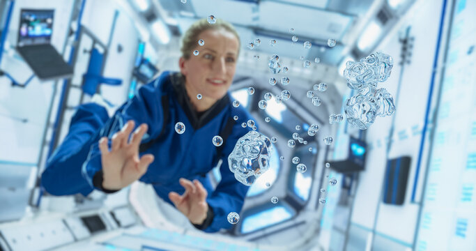 Female Cosmonaut in a Blue Suit Interacts With Floating Water Droplets Inside a Space Station, Demonstrating gravity Effects. Portrait of a Courageous Female Astronaut on Board a Spacecraft, Floating