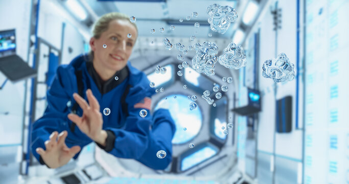 Female Cosmonaut in Blue Suit Interacts With Floating Water Droplets Inside a Space Station. Portrait of a Courageous Female Astronaut. Space Travel, Solar System Exploration and Colonization Concept