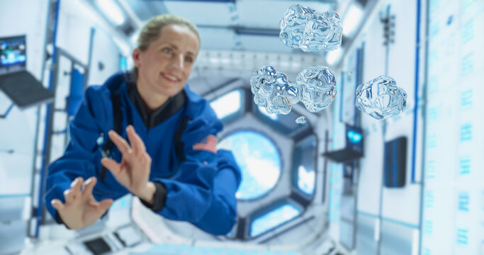 Female Cosmonaut in a Blue Suit Interacts With Floating Water Droplets Inside a Space Station, Capturing the Unique Behavior of Liquids in Microgravity