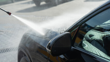 A self-service car wash featuring a high-pressure water spray cleaning a vehicle. Active foam...