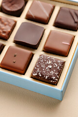 Minimal flatlay of open box with chocolate squares on beige background, elegant candy dessert packaging mockup concept