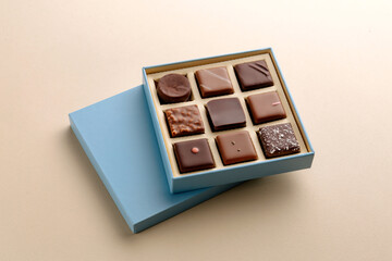 Minimal flatlay of open box with chocolate squares on beige background, elegant candy dessert packaging mockup concept