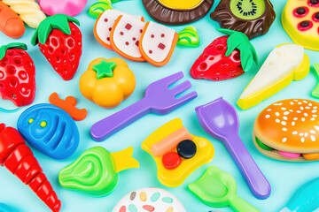 Synthetic plastic fruits and candies stacked chaotically on soft blue surface, emphasizing artificial eating habits