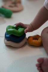 A baby"s hand stacks colorful, irregularly shaped toys on a light surface, promoting sensory play and early childhood development.