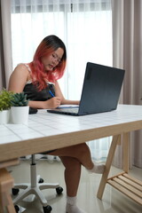 A woman with red hair is sitting at a desk with a laptop and a pen