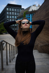 Stylish tech-savvy woman in black outfit posing in urban architecture – lifestyle shoot