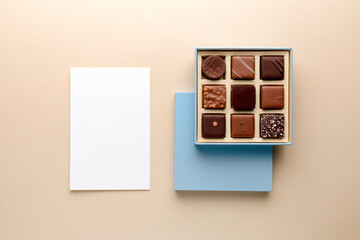 Minimal flatlay of open box with chocolate squares and blank card on beige background, elegant candy dessert packaging mockup concept