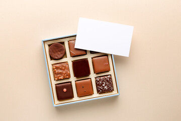 Minimal flatlay of open box with chocolate squares and blank card on beige background, elegant candy dessert packaging mockup concept