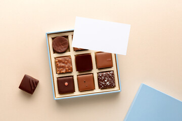Minimal flatlay of open box with chocolate squares and blank card on beige background, elegant candy dessert packaging mockup concept