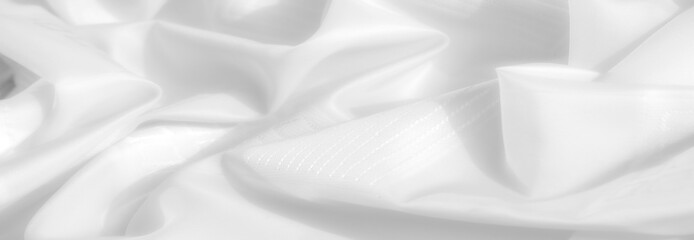 Obraz premium soft white fabric laid out in a relaxed manner, creating gentle curves and ripples. The fabric appears slightly translucent, revealing a subtle texture in the weave. Light plays across the surface