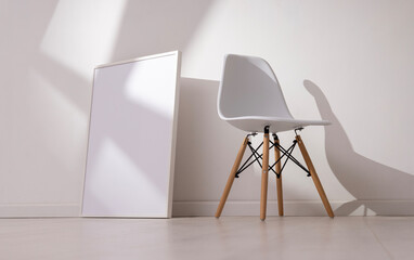Mockup of empty frame in modern minimalist interior with chair and morning light on white wall background. Template for artwork, painting, photo or poster